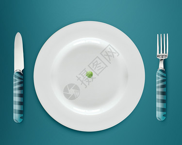白盘上的绿色豆子和蓝底的刀叉概念厨房陶瓷图片