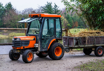 农艺学村汽车业设备橙色拖拉机和装满干草农用机械的拖车图片