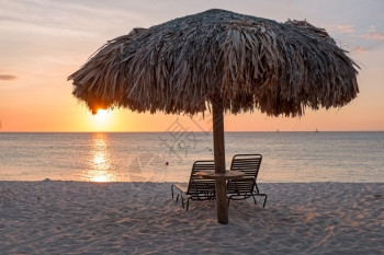 目的地日落时阿鲁巴岛海滩的草伞雨旅行背景图片