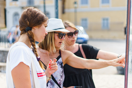 观光团体3名女旅游客在假期的暑日观看科孚镇旅游目的地信息板上图点在度假时观看Corfu镇旅游目的地信息板上图位置科孚岛图片