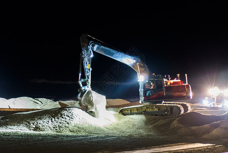 舀机械土方工程夜间在黑暗中工作的地面人用挖掘机将沙移到海滩进行维护在夜间工作图片