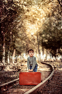 孩子玩穿着旧衣服的可爱小男孩站在废弃铁路上手里拿着旧式提箱的行李色调图片