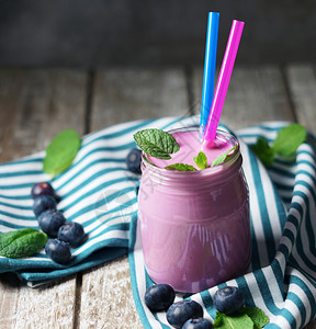 早餐食物健康杯子里的蓝莓新鲜凉冰奶昔两根饮料稻草和薄荷叶黑色生锈背景和一张木桌图片