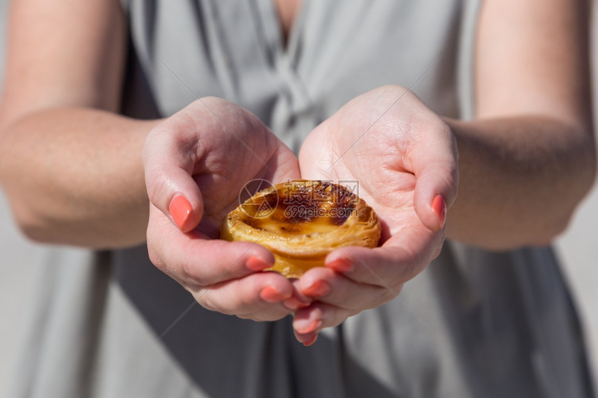 游客甜点糊状在葡萄牙里斯本的背景点上葡萄牙传统妇女手中的Pasteisdenataspathes图片