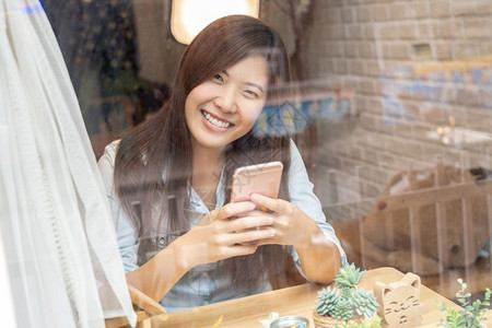 社会的咖啡亚洲女商人手使用智能移动电话在工作场所或合用办公空间现代室商业生活方式概念的玻璃边桌子上采取幸福行动利用智能手机和快乐图片