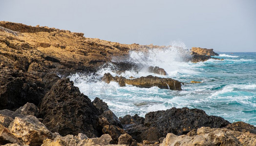 海浪撞击塞浦路斯岛卡帕阿波托洛安德列亚海滩的岩石泡沫天空支撑图片