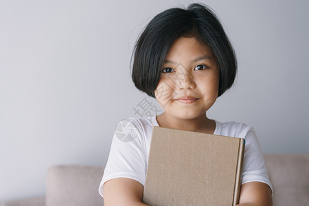 亚洲小女孩拿着一本棕色的书站在家中客厅里时微笑着容人们放松孩子图片