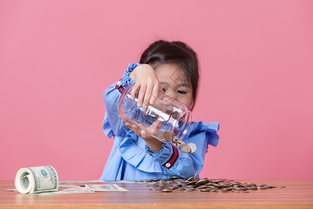 未来女幸福这小孩从一个透明的玻璃罐中将硬币倒在地上金钱储蓄的概念图片