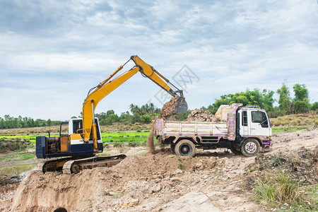 自卸车污垢伊拉克黄色挖掘机将土壤装入建筑工地的倾卸卡车中图片