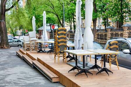 危机空的在封闭夏季咖啡馆木制平台上有花园家具桌椅子和雨伞在城市街道和过往汽车的背景下被捆绑在一起户外咖啡厅室区域被关闭户外家具桌图片