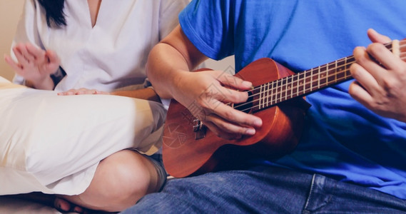 幸福歌曲年轻的情侣在床上弹Ukulele和吉他图片