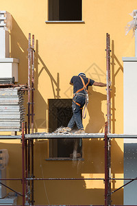 修理男家戴蓝色安全帽的工人在建筑地的脚手架上作一名建筑人在地的脚手架上作图片