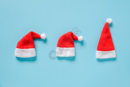 三件红色圣诞老人礼帽蓝色背景的红脸卡片布局顶端视图平板模用于设计卡片请帖冬季假日构成三个红色圣诞老人礼帽子蓝色背景的红纸牌布局顶图片