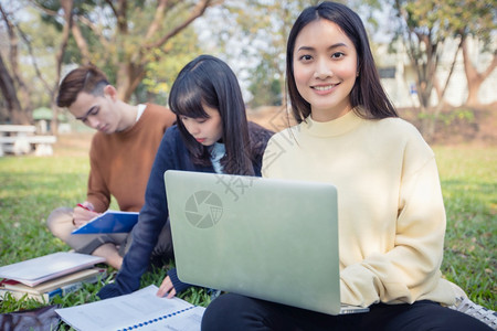 电脑学生坐在绿色草地上一起学习的学生们背景