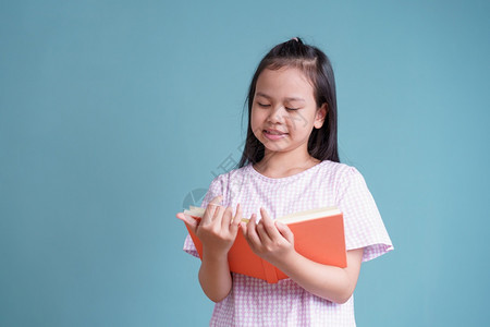 亚洲快乐的小女孩站着阅读书关于蓝背景孤立的色复制室内的在家工作图片