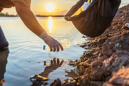 在日落的河边将垃圾塑料瓶装在黑袋中的志愿者生态橡胶的图片