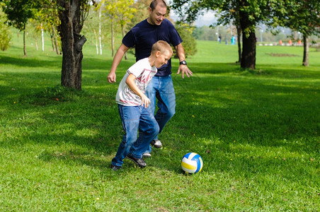 爸爸带着孩子在户外踢球图片