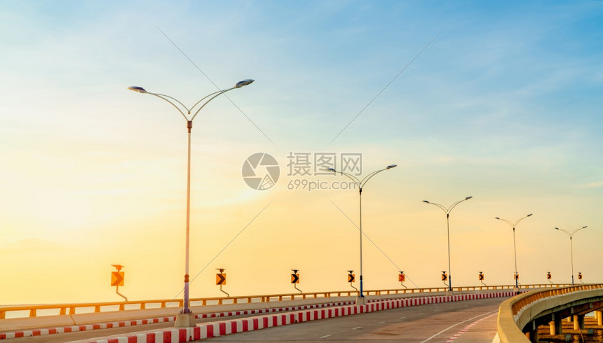 日落时在海边有曲线和人行道交通标志的曲线混凝土道路黄色曲线交通标志上的太阳能电池板源暑假公路旅行红白交通标志城市车辆日出图片