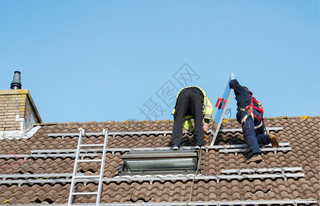 把太阳能电池板安装在屋顶上的工人图片