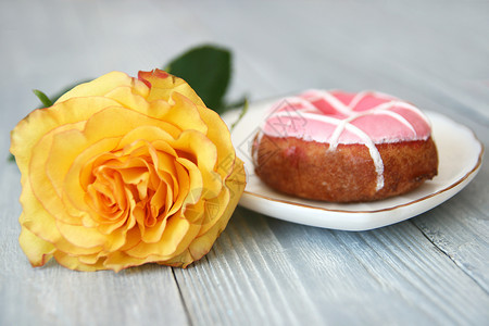 惊喜一朵美丽的黄玫瑰有开着的芽和甜圈白陶瓷板上有粉红冰淇淋灰色木质背景空间母亲面粉图片