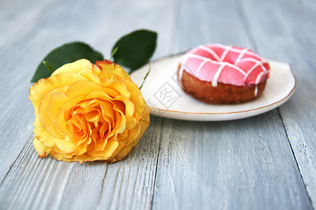 一朵美丽的黄玫瑰有开着的芽和甜圈白陶瓷板上有粉红冰淇淋灰色木质背景空间自然卡片爱图片