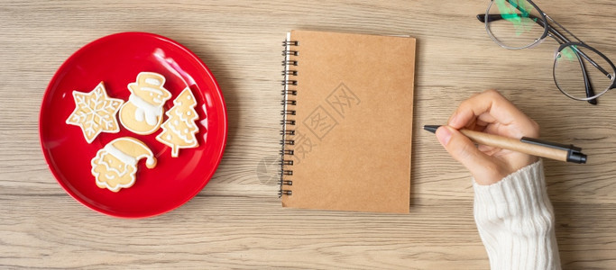 时间妇女手写笔记本在表格Xmas新年快乐目标决议清单战略和计划概念上用圣诞饼干写字刨冰日历图片