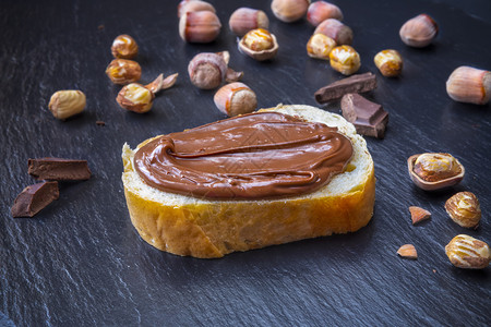 新鲜的一顿饭面包片巧克力奶油和黑桌上的栗子提供美味早餐概念重点在面包上巧克力奶油面包上胡桃甜饼点图片