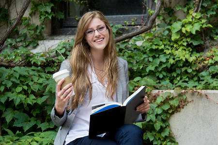 坐在花坛边一边喝咖啡一边看书的女性图片