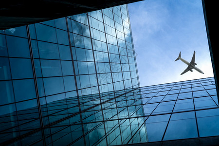 飞机在现代玻璃办公楼上空飞行未来商务建筑的透视图摩天大楼建筑外部商务旅行透明玻璃窗中的反射航空外部的底商业图片