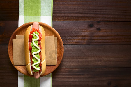 制作由面包香肠番茄鳄梨和蛋黄酱构成的智利意大传统热狗三明治用自然光选择焦点在黑木头上拍摄了照片以天然光为焦点关注热狗卷的图片