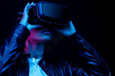 虚拟的年轻播放器身着眼镜的非裔美国年轻女子观看360度视频其虚拟现实头盔在亮光中的黑色背景上被隔离注图片