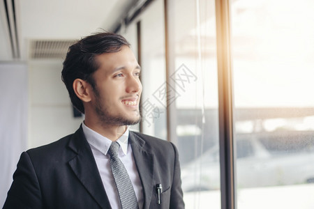 在职的快乐英俊商人站着微笑在办公室里肖像套装图片