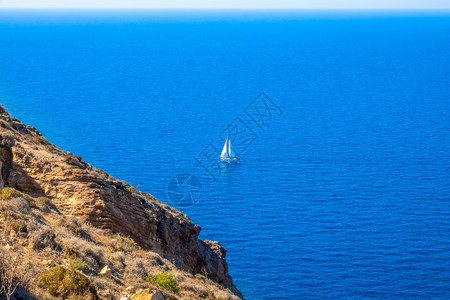 在蓝海克里夫伊岸和蓝航行游艇上孤单帆船在蓝海航行游艇石头悬崖旅行图片