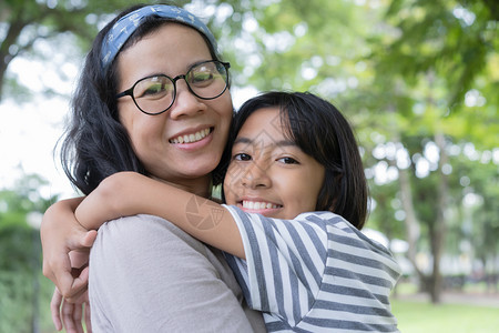 闲暇脸年轻的亚裔母亲与女儿拥抱彼此在公园微笑对方快乐家庭概念图片