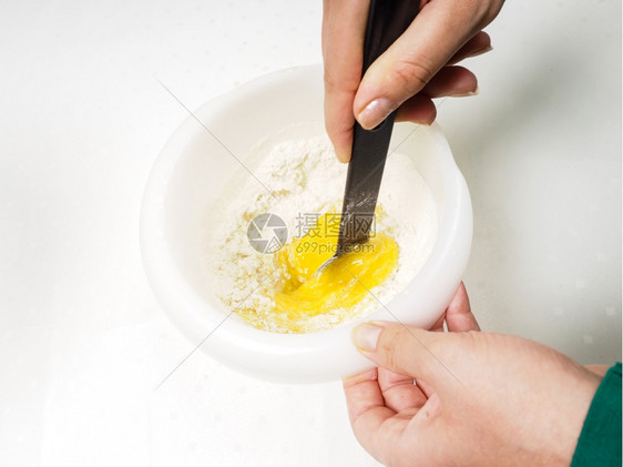 女将面粉与蛋黄和熔奶油混合在一起塑料碗中用黑块浆混在一起糖盘子融化了图片
