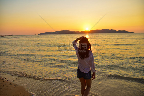 美丽的放松站在海边滩上的妇女在晚金时日落的背景下在泰国旅行暑假沙滩上站着图片