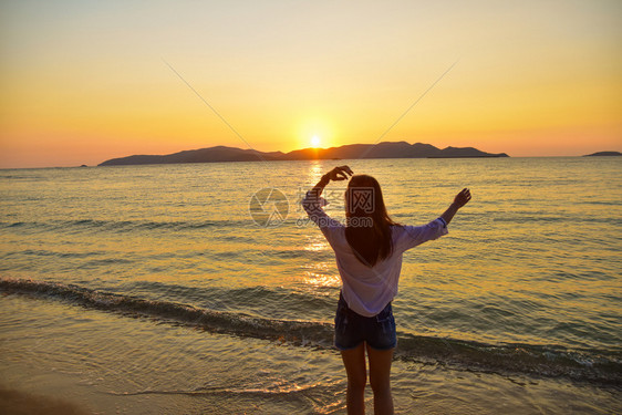 女孩自然水站在海边滩上的妇女在晚金时日落的背景下在泰国旅行暑假沙滩上站着图片