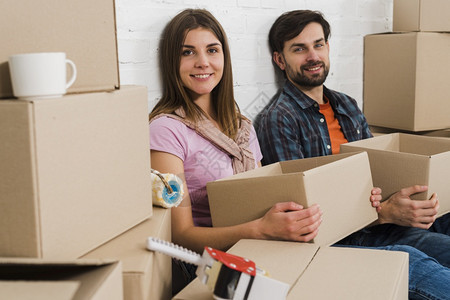 在室内真实的微笑年轻夫妇拿着纸板盒在放松新房子盒背景图片