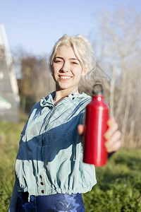 运动合身坐在户外的快乐女跑步者拿着水瓶和笑微的健康女人在身后休息活动图片