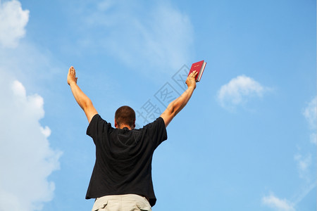祈祷年轻男人与举起的手站在蓝天上情绪化的逗留图片