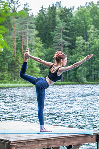 瑜伽标识摆姿势景观体式年青瑜伽女Natarajasana的变异在健康生活和自然平衡概念湖边跳舞波斯领主背景