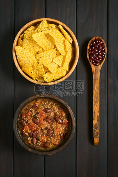 煮熟的肉黑暗用木制勺子上含干肾豆的碗中辣椒粉和玉米饼片头照用天然光在黑木上图片