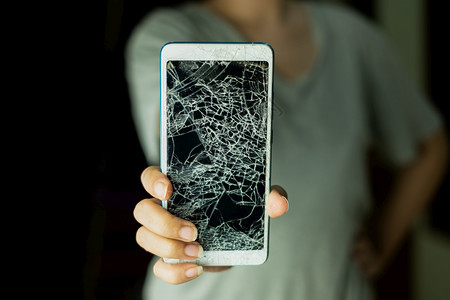 皲裂事故聪明的女人站着拿智能手机的屏幕黑背景被打碎了图片