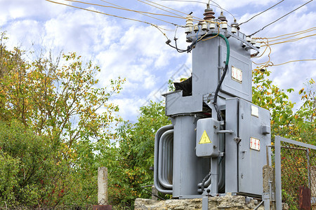 行业电缆一个古老的变压器电站在秋天花园的中间一个用金属网格围住的秋天花园与蓝云空变换器电站对面压器电站在花园中央一个蓝色云层对面背景图片