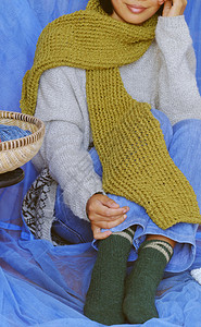 白色的自由温暖妇女穿着蓝色牛仔裤白羊毛衫袜子和苔绿色羊毛围巾与蓝背景坐在一起编织手工制作产品为业余爱好冬季取暖图片