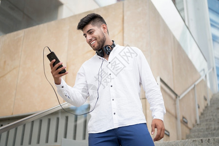 信心市中年轻英俊的西班牙裔男子在户外使用智能手机高质量照片年轻英俊的西班牙裔男子在户外使用智能手机微笑图片