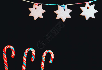 戳糖果万圣节棒甘蔗和挂着姜饼干以恒星的形状印在黑色背景上请用贺卡假日背景并有空间复制与甜一起的节日背景图片