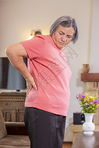 白种人疼痛家中患有背的女年长妇用手往下反按摩感到疲惫站在起居室里累图片