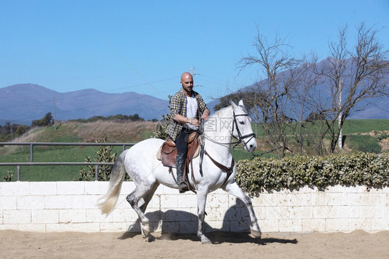 在沙地上骑白马的穿散装年轻人垂直训练骑师图片