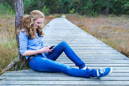 人行道信息白种女孩坐在木脚上自然界打呼唤手机称图片